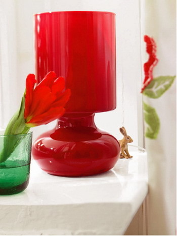 En lille bordlampe fra et blæst glas (IKEA) fylder rummet med et varmt rødligt lys. Lysekrone lavet af akryl og glas (Kare Design, Tyskland) - en af ​​de lyse accenter i interiøret